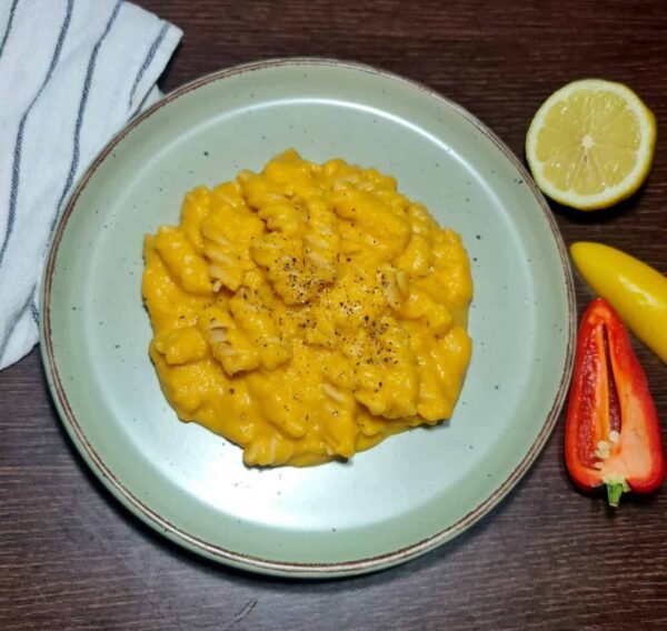 Fresh butternut squash, onion, garlic, lemon, olive oil, spices, and plant milk on a dark table.