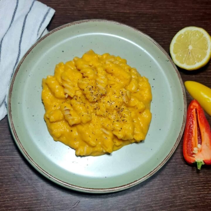 Fresh butternut squash, onion, garlic, lemon, olive oil, spices, and plant milk on a dark table.