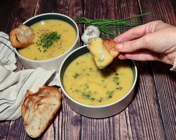 Two bowls of cheap potato leek soup topped with chives and served with toasted bread.