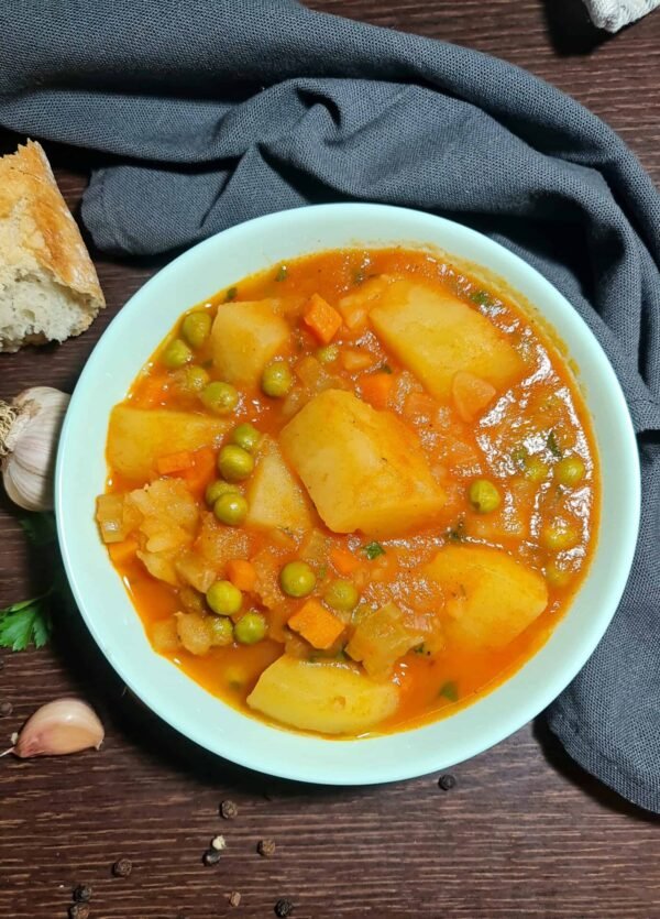 Extreme close-up of a bowl of chunky potato and peas soup, showing the large potato pieces, bright green peas, and thick tomato broth.