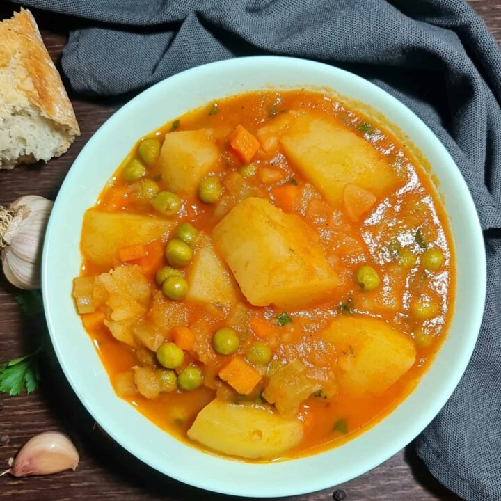 Extreme close-up of a bowl of chunky potato and peas soup, showing the large potato pieces, bright green peas, and thick tomato broth.