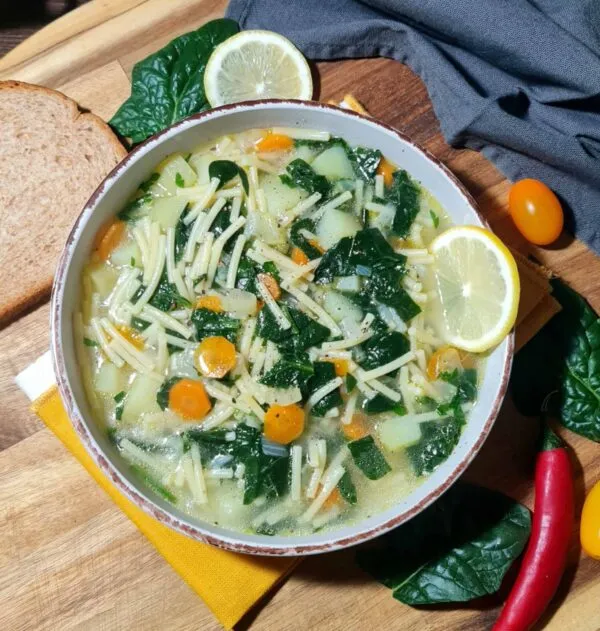 Extreme close-up of the light broth of spinach noodle soup, highlighting the thin noodles, chopped spinach, and a slice of lemon garnish.