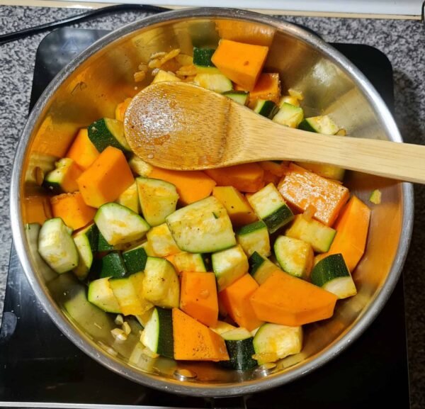 Pumpkin and zucchini chunks cooking in a pot with onions and garlic.