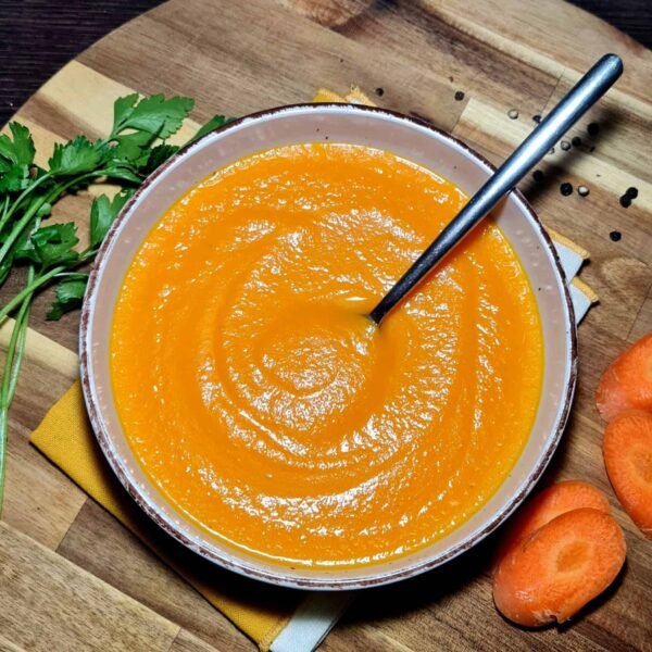 Bowl of creamy carrot soup served on wooden board with fresh carrots
