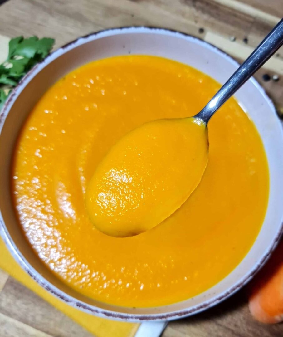 A bowl of creamy carrot soup with a spoon showing its smooth and velvety texture