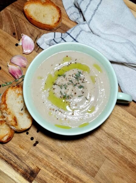 Overhead shot of creamy cauliflower and chestnut soup drizzled with olive oil and topped with thyme and black pepper.