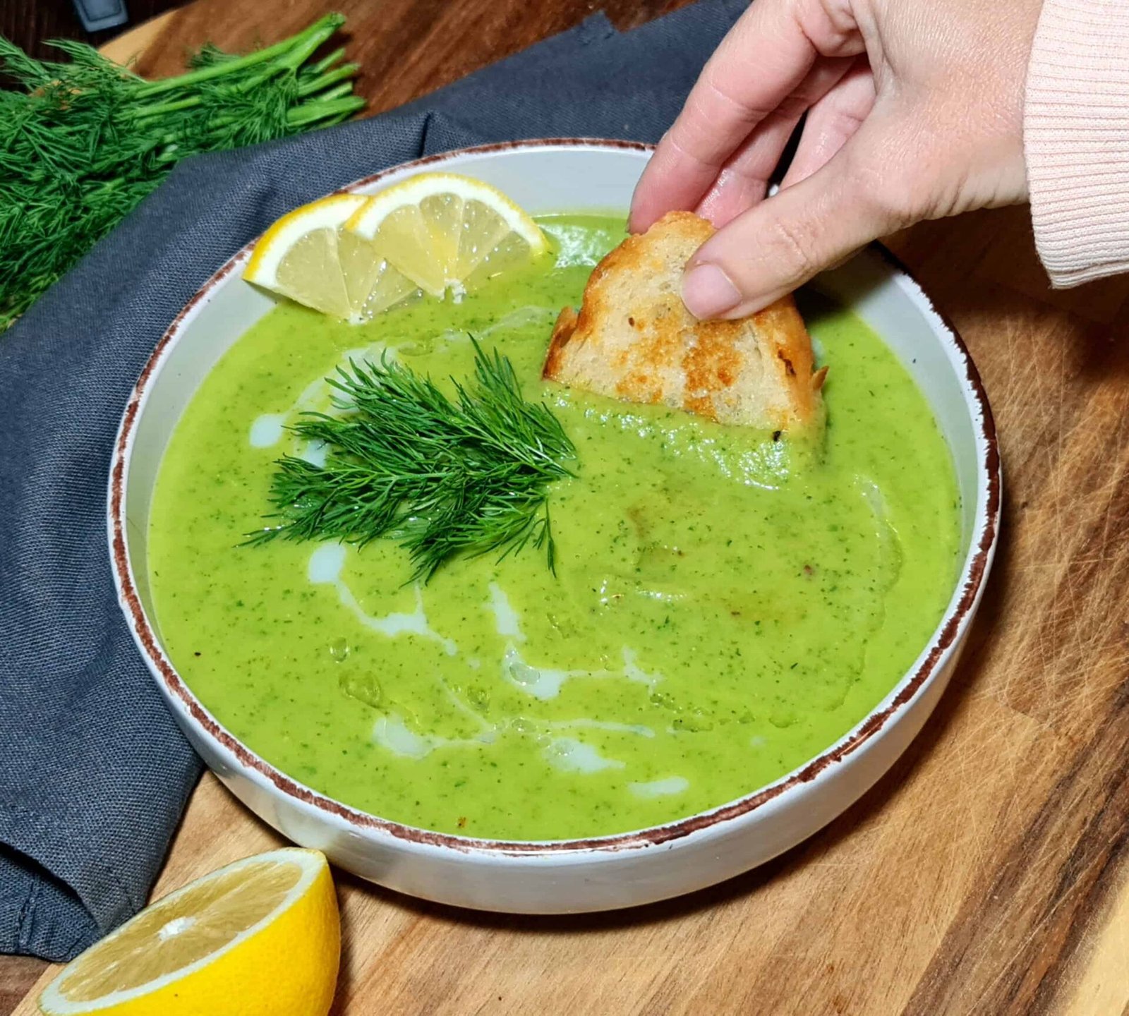 Close-up of a spoonful of creamy green soup with fresh dill and lemon in the background.