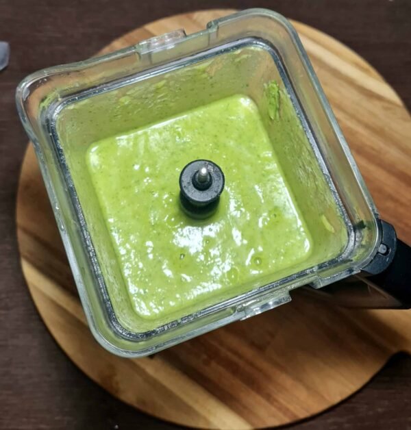 Thick green soup being blended into a smooth purée inside a blender.