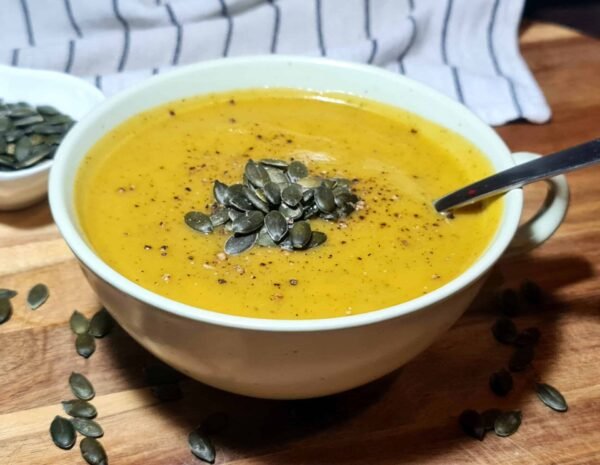 Side view of creamy pumpkin zucchini soup with pumpkin seeds and a spoon resting in the bowl.