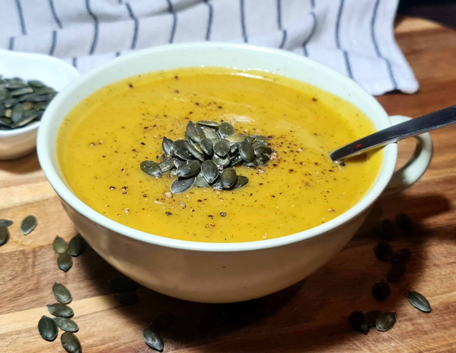 Side view of creamy pumpkin zucchini soup with pumpkin seeds and a spoon resting in the bowl.
