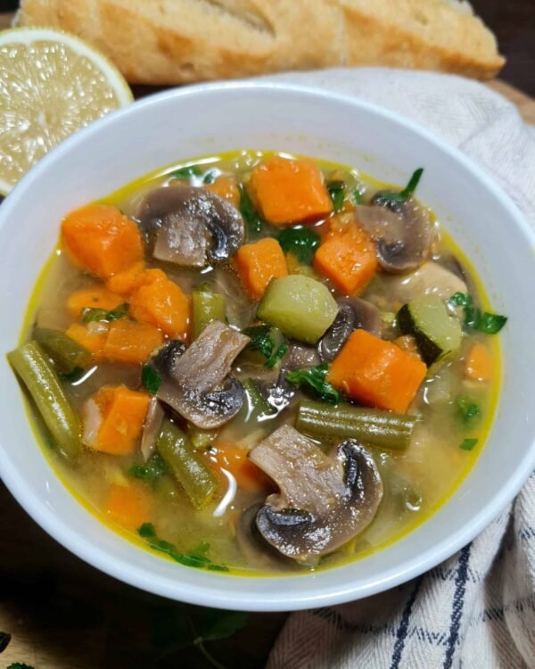 Cozy bowl of easy vegetable soup with mushrooms, sweet potato, zucchini, and green beans, served with lemon and baguette.