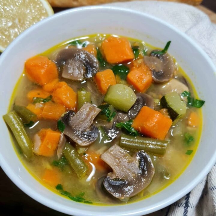 Cozy bowl of easy vegetable soup with mushrooms, sweet potato, zucchini, and green beans, served with lemon and baguette.