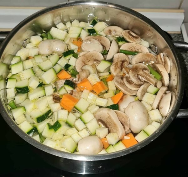 Pot filled with raw zucchini, sweet potato, mushrooms, and green beans in water before simmering for easy vegetable soup.