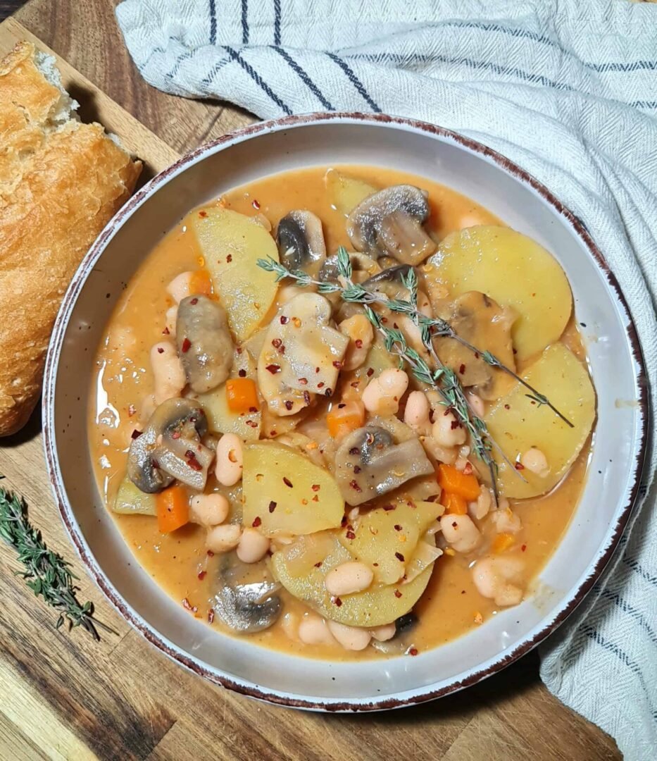 vegan white bean mushroom soup served with crusty bread and thyme sprig
