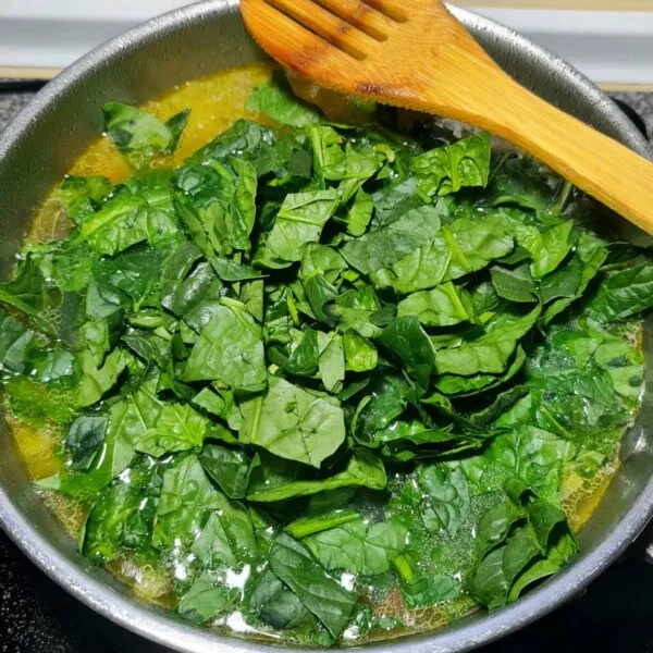 Large pile of fresh spinach leaves added to the hot broth in the pot, beginning to wilt down for the spinach noodle soup.