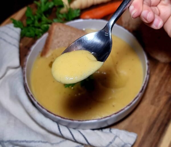 Close-up of a spoonful of silky Irish vegetable soup, showing its smooth, creamy texture above a bowl of freshly blended soup.