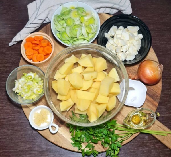 Overhead view of chopped potatoes, leeks, carrots, parsnips, celery, garlic, onions, parsley, and oil prepared for Irish vegetable soup.
