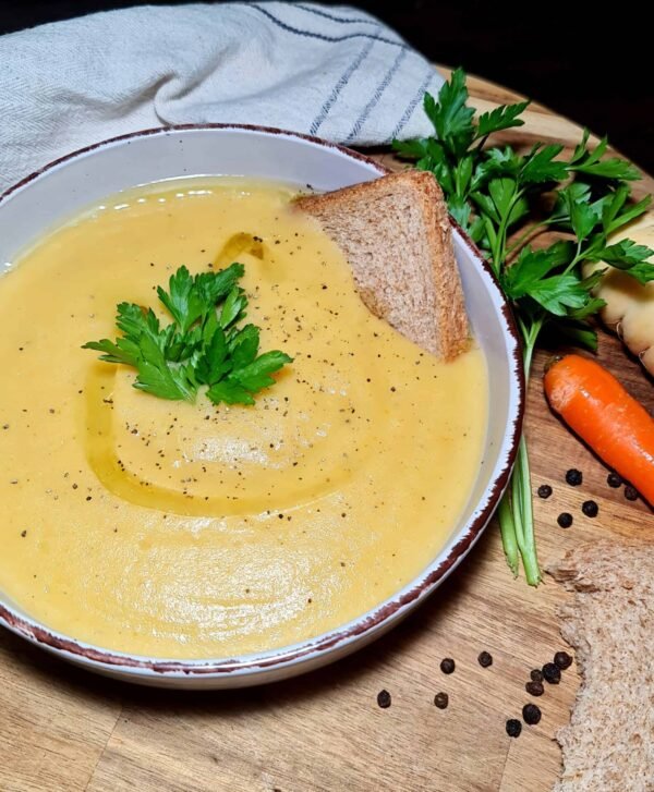 Side angle photo of a bowl of Irish vegetable soup with parsley and bread on a wooden board.