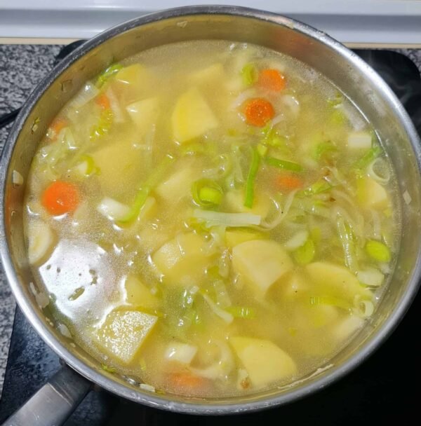 Pot filled with potatoes, leeks, carrots, and broth simmering to make Irish vegetable soup.