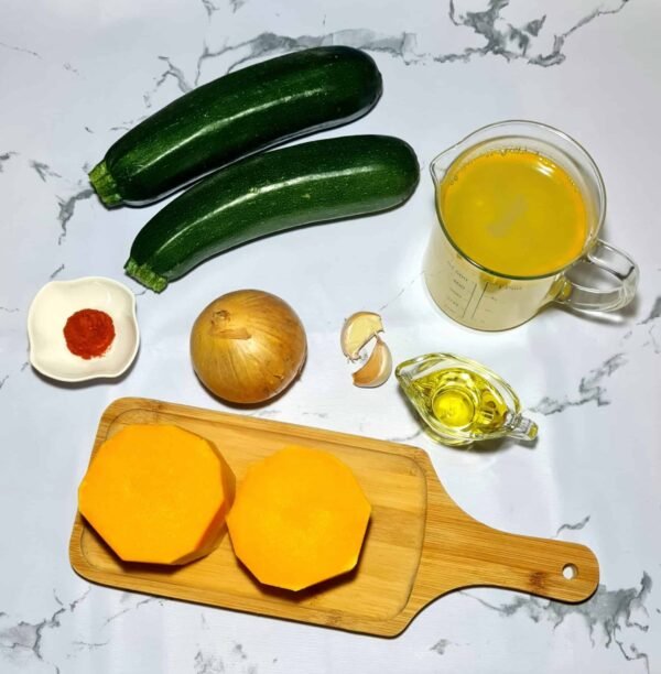 Raw ingredients for pumpkin zucchini soup including pumpkin, zucchini, onion, garlic, olive oil, and spices.