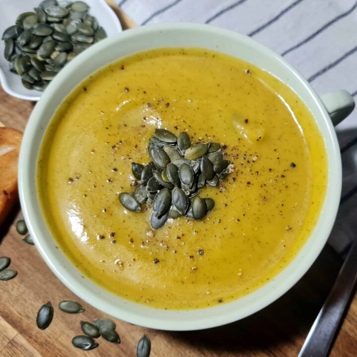 Top view of creamy pumpkin zucchini soup garnished with pumpkin seeds and black pepper.