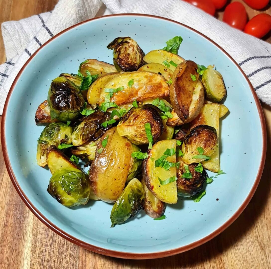 A close-up view of roasted Brussels sprouts and potato wedges, lightly charred and sprinkled with fresh parsley.