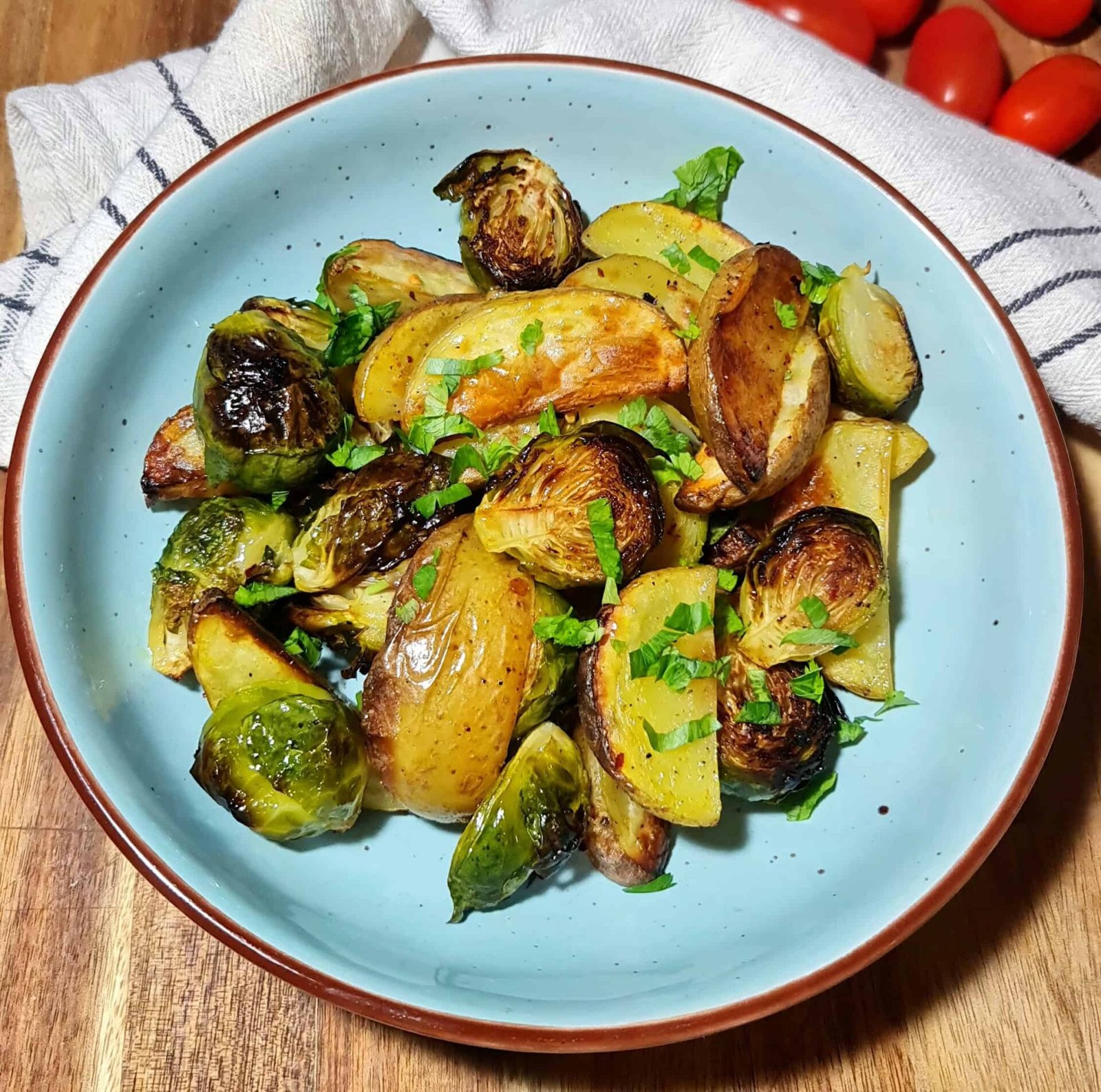 A close-up view of roasted Brussels sprouts and potato wedges, lightly charred and sprinkled with fresh parsley.