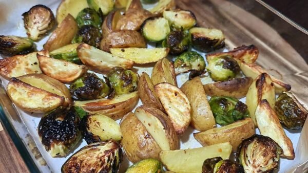 Freshly roasted Brussels sprouts and potatoes in a baking dish with charred edges.