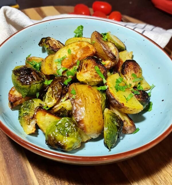 Angled shot of a bowl filled with roasted Brussels sprouts and potatoes garnished with parsley.
