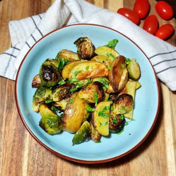Overhead shot of roasted Brussels sprouts and potatoes served in a blue bowl on a wooden board.