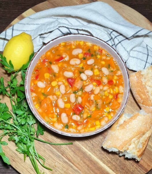 Overhead shot of a rustic bowl filled with chunky vegan bean and corn soup, garnished with fresh parsley, on a dark wooden background.