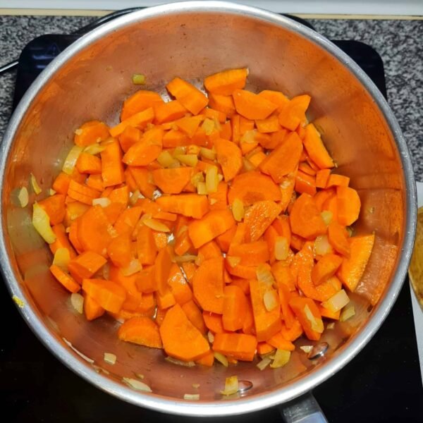 Chopped carrots and onions sautéing in a pot for carrot soup
