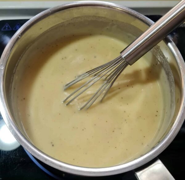 Creamy vegan béchamel in a pot with a whisk, made from plant milk, flour, and spices.