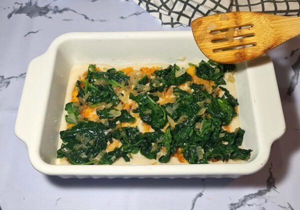 Cooked spinach and onions layered over creamy pumpkin in a white baking dish.