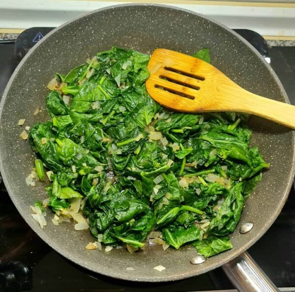 Fresh spinach sautéed with onion and garlic in a pan for vegan pumpkin spinach lasagna.