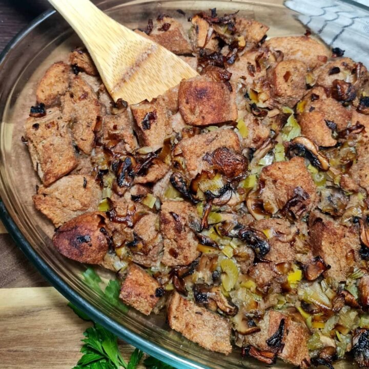 Mixing sautéed vegetables with bread cubes in a bowl for vegan stuffing.