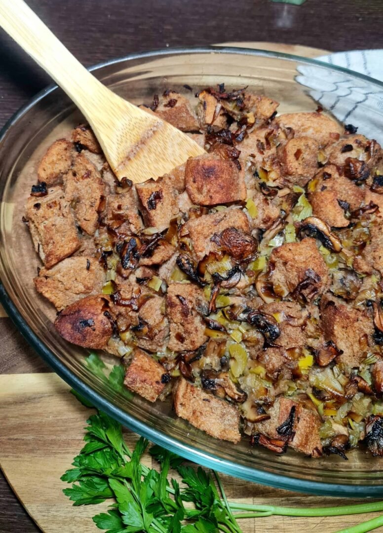 Mixing sautéed vegetables with bread cubes in a bowl for vegan stuffing.