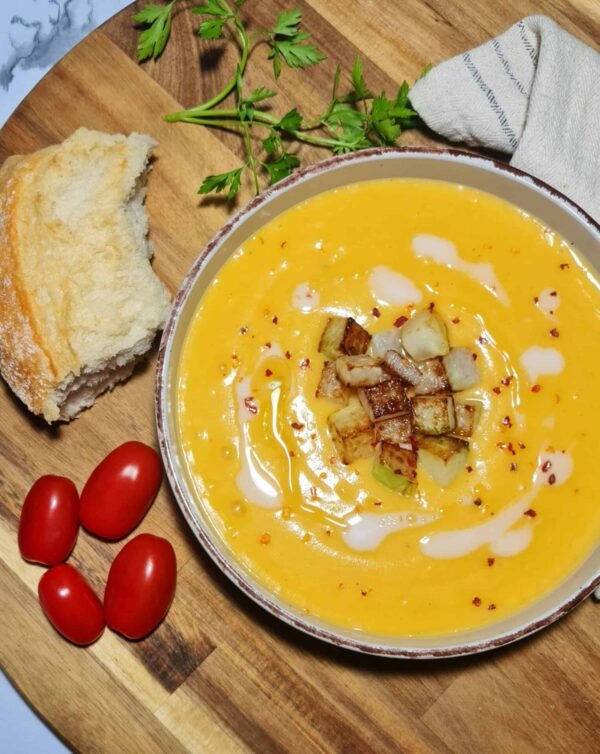 A bowl of creamy winter kohlrabi soup with crispy cubes in the center, served with rustic bread and parsley.