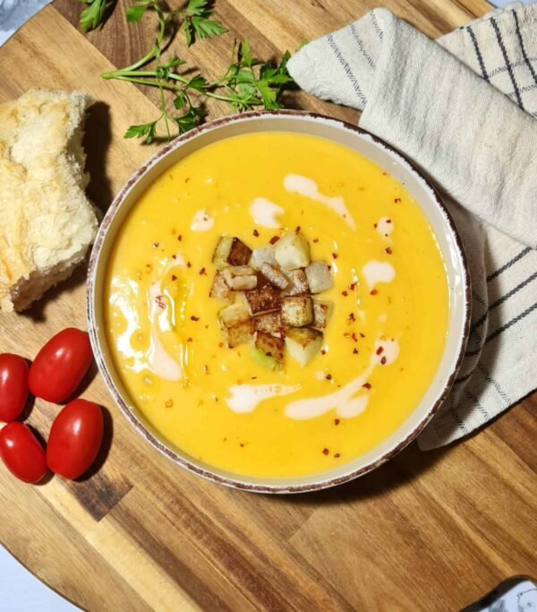 Overhead view of a bowl of creamy winter kohlrabi soup topped with browned kohlrabi cubes, coconut cream swirls, and red pepper flakes.
