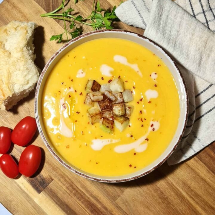 Overhead view of a bowl of creamy winter kohlrabi soup topped with browned kohlrabi cubes, coconut cream swirls, and red pepper flakes.